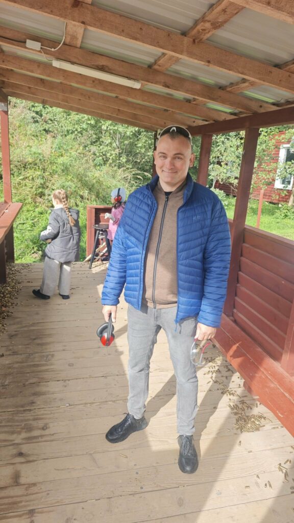 Asociacijos „Kas vyksta Kuršėnuose“ vadovas Andrius Gagys Praktinio šaudymo centre, įgyvendinant projektą „Šiaulių rajono gyventojų pilietinio pasirengimo ir informavimo stiprinimas“. Rankose laiko apsaugines ausines ir akinius.