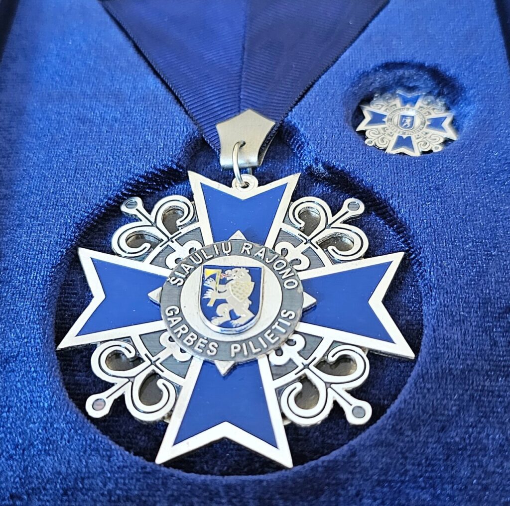 Šiaulių rajono garbės piliečio ženklas mėlyname dėkle.