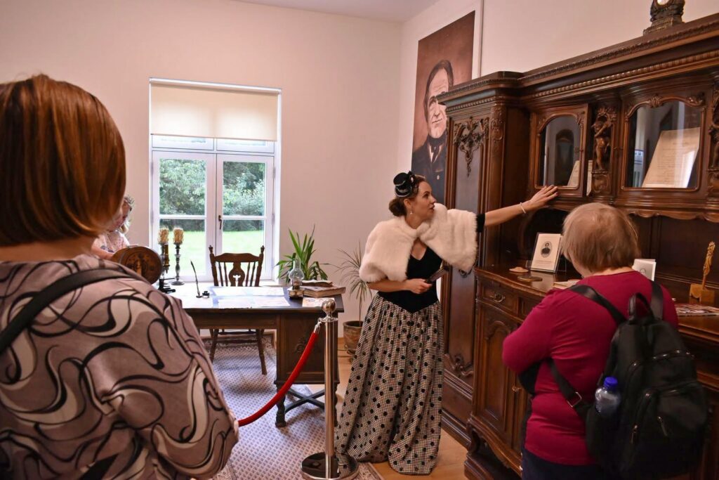 Kultūrinės veiklos vadybininkė-gidė Daiva Daknienė Kuršėnų dvare ekskursijos metu pristato dvaro interjero detales ir pasakoja apie čia gyvenusių žmonių kasdienybę.