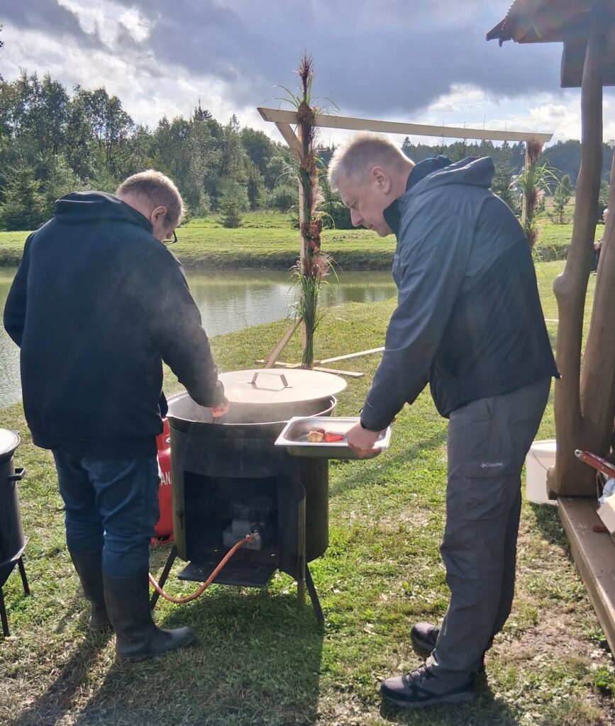 Du vyrai prie Noreikių bendruomenės tvenkinio ruošia maistą dideliame kazane per „Rudens bendrystės šventę“.
