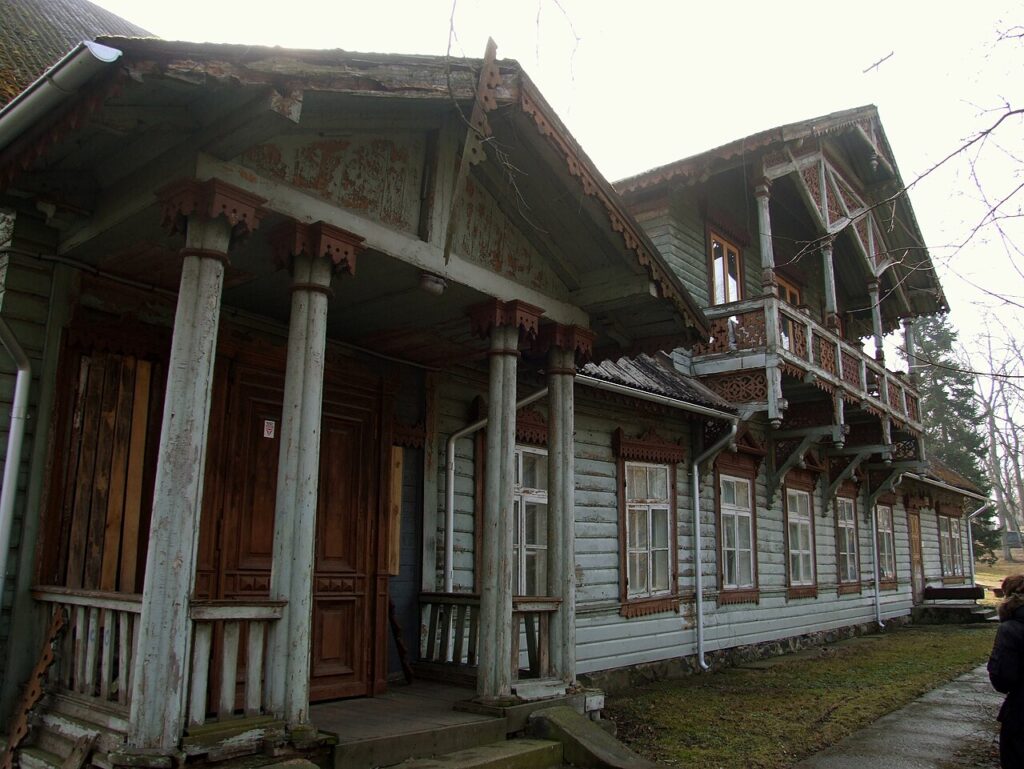 Kuršėnų Gruževskių dvaro rūmai prieš restauraciją – senasis medinis pastatas su puošybos elementais ir veranda.