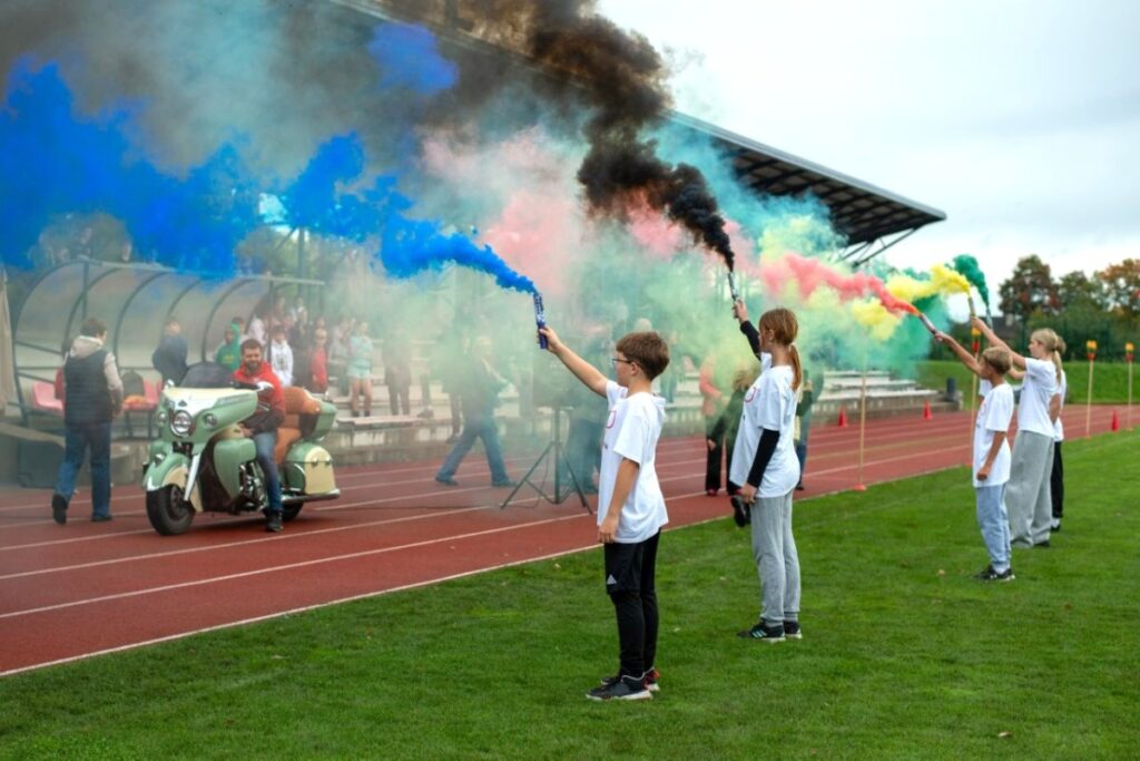 „Olimpinio rudens 2026“ atidarymo akimirka Kuršėnų stadione – mokiniai su spalvotų dūmų fakelais.