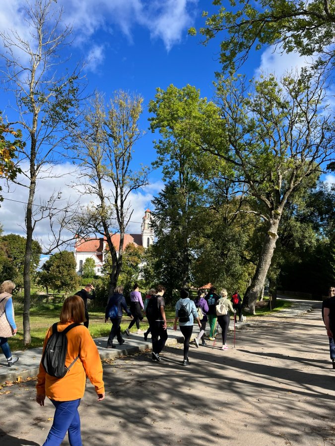 Europos paveldo dienų žygio dalyviai eina per Kurtuvėnus, fone matyti Kurtuvėnų Šv. apaštalo Jokūbo bažnyčia.